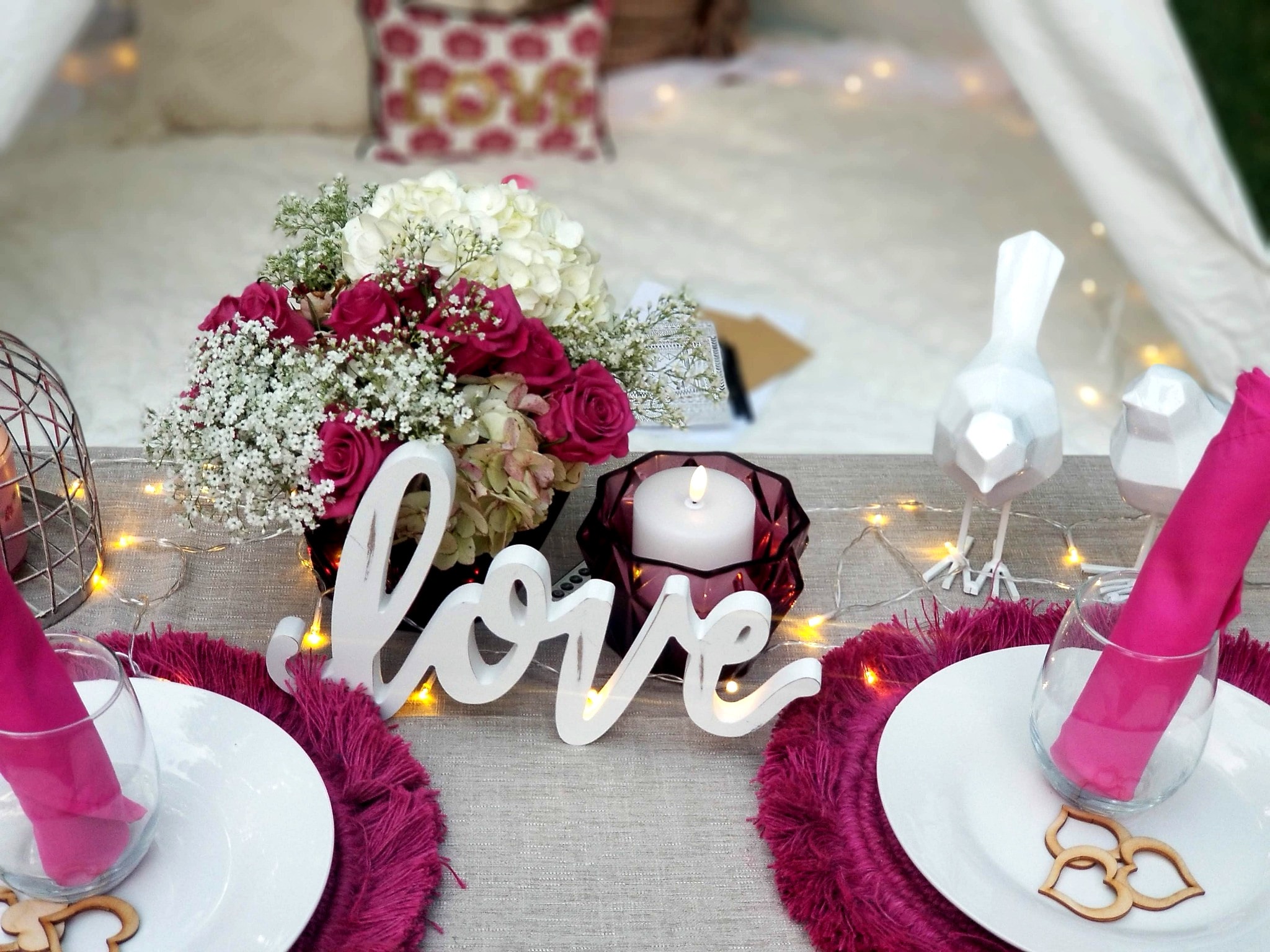 Romantic outdoor tablescape with magenta roses, love sign, and fairy lights